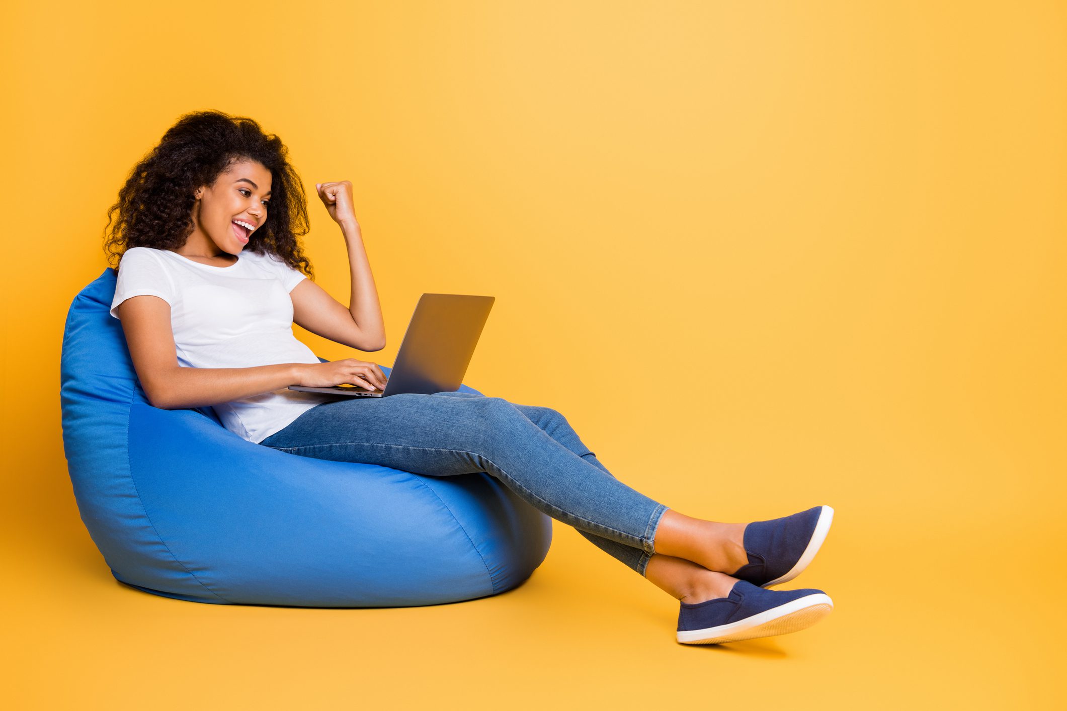 Portrait-of-nice-attractive-lovely-cheerful-cheery-glad-satisfied-wavy-haired-girl-sitting-in-bag-chair-using-laptop-celebrating-isolated-over-bright-vivid-shine-vibrant-yellow-color-background
